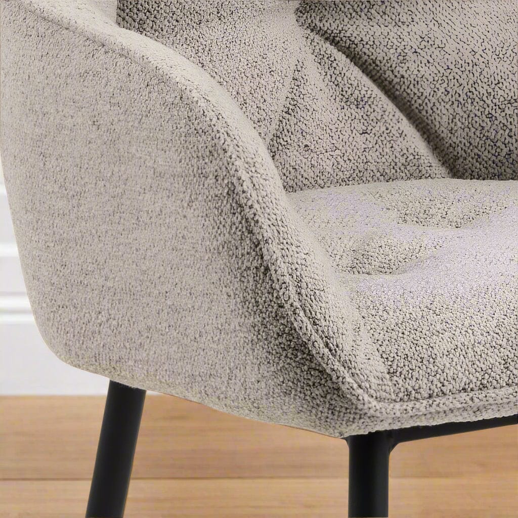 "Beige dining chair with armrests, soft bouclé fabric, tufting detail, and black powder-coated steel legs, perfect for modern dining spaces."
