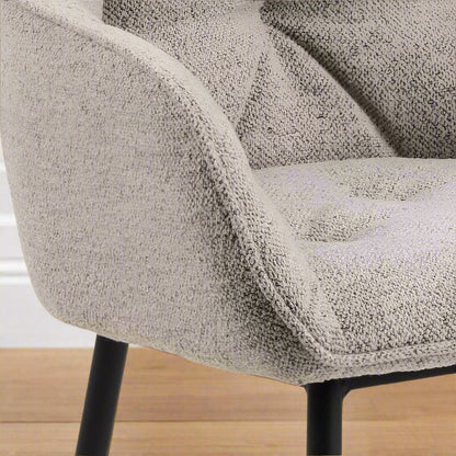 "Beige dining chair with armrests, soft bouclé fabric, tufting detail, and black powder-coated steel legs, perfect for modern dining spaces."