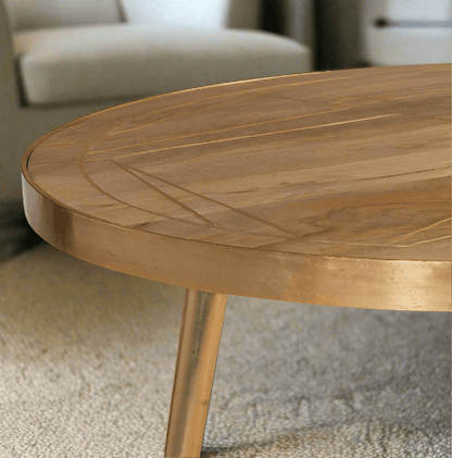 Round coffee table with gold metal inlays on the solid mango wood top, gold metal frame around the edge, and three angled metal legs, in a light natural finish.
