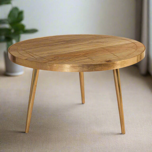 Round coffee table with gold metal inlays on the solid mango wood top, gold metal frame around the edge, and three angled metal legs, in a light natural finish.