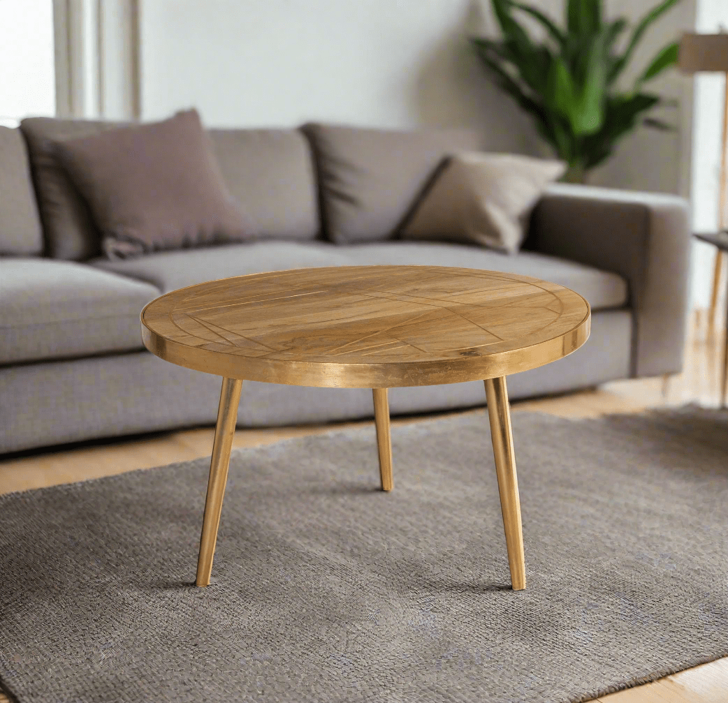 Round coffee table with gold metal inlays on the solid mango wood top, gold metal frame around the edge, and three angled metal legs, in a light natural finish.