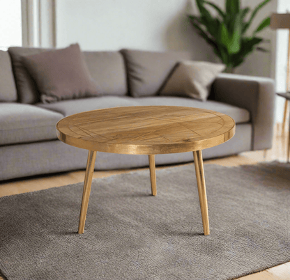 Round coffee table with gold metal inlays on the solid mango wood top, gold metal frame around the edge, and three angled metal legs, in a light natural finish.