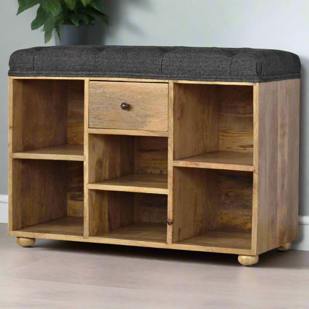 Small shoe storage bench with oak-ish finish, black tweed upholstered seat, 1 drawer with shiny knob, 6 open shelves, and 4 bun feet.