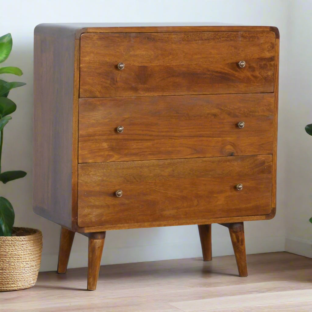 "Curved chest of drawers made from solid mango wood with chestnut finish, featuring shiny accent knobs, four Nordic-style legs, and smooth, rounded corners for a modern, contemporary look."