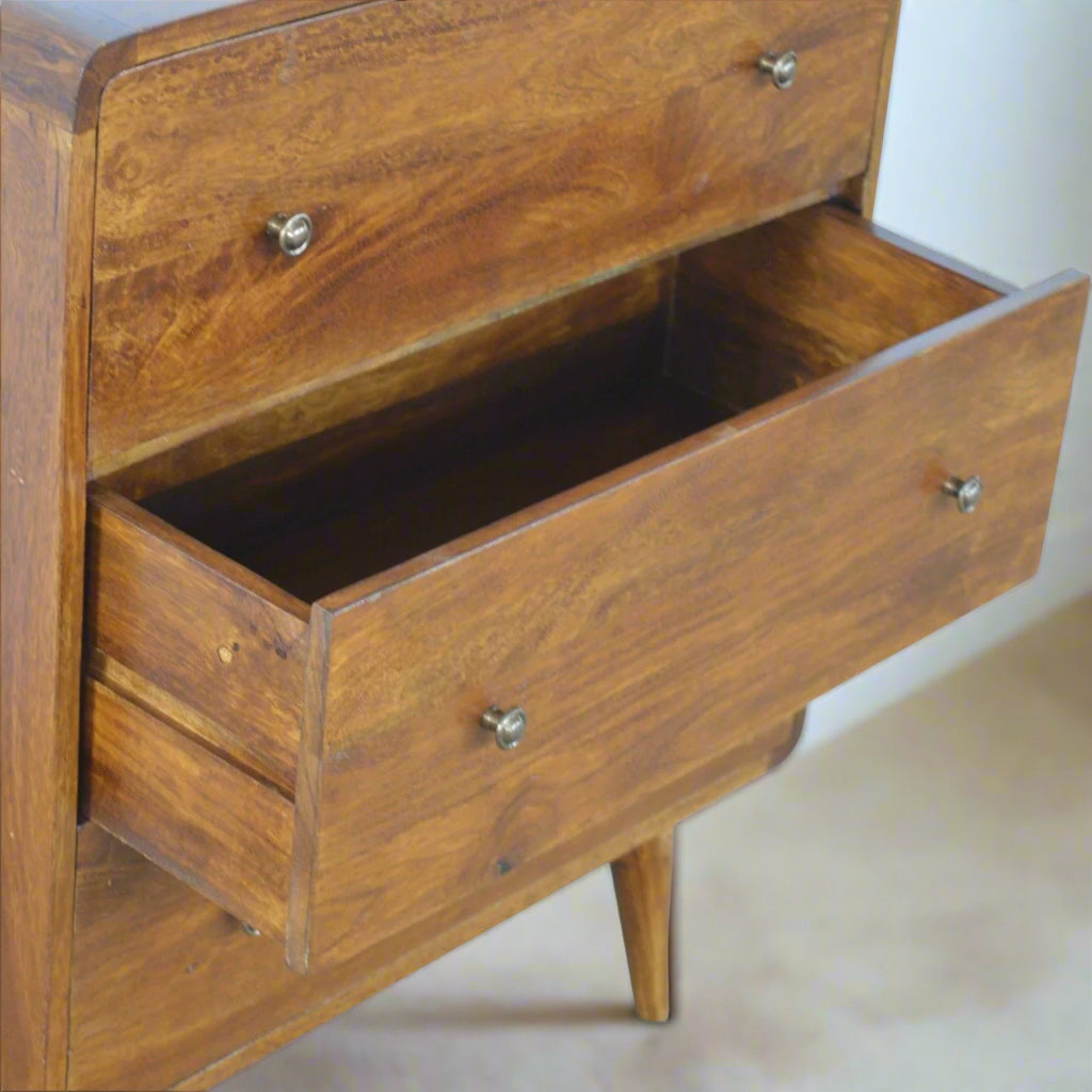 "Curved chest of drawers made from solid mango wood with chestnut finish, featuring shiny accent knobs, four Nordic-style legs, and smooth, rounded corners for a modern, contemporary look."