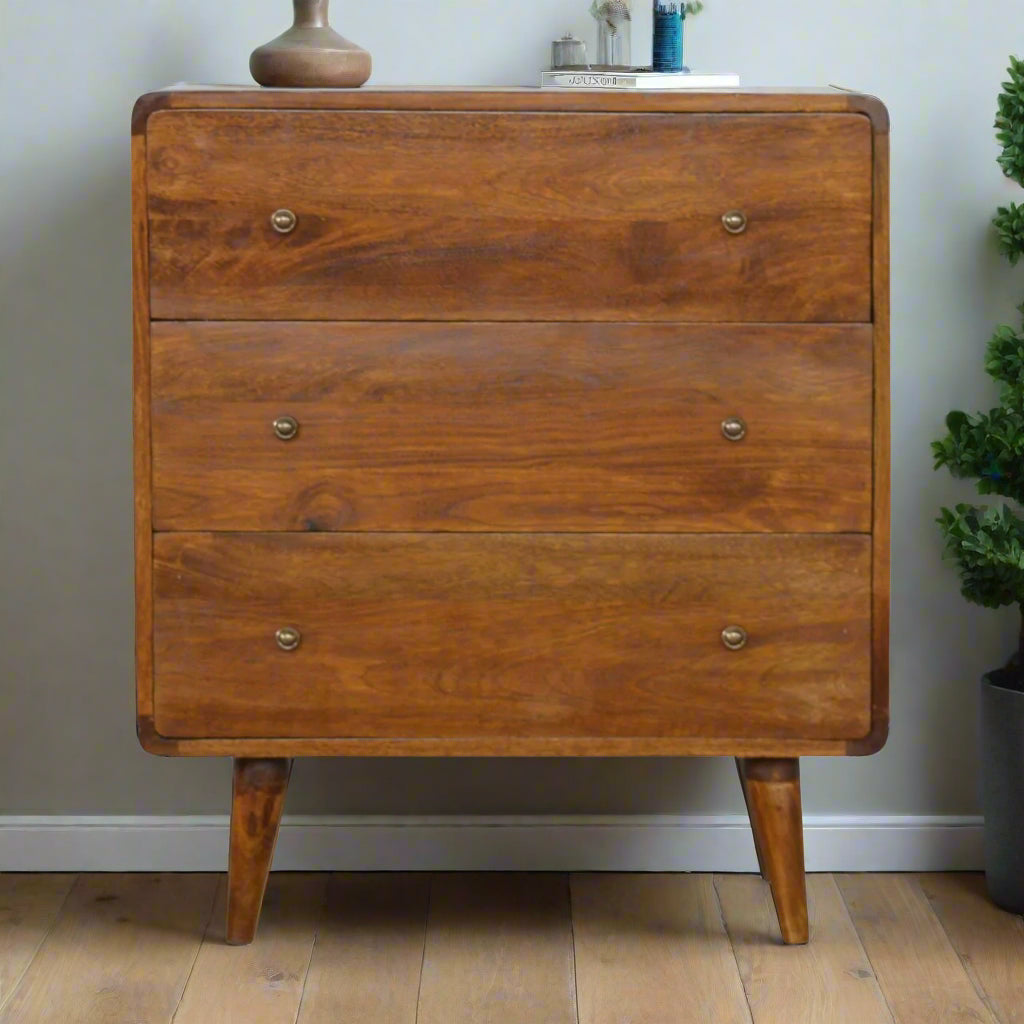 "Curved chest of drawers made from solid mango wood with chestnut finish, featuring shiny accent knobs, four Nordic-style legs, and smooth, rounded corners for a modern, contemporary look."